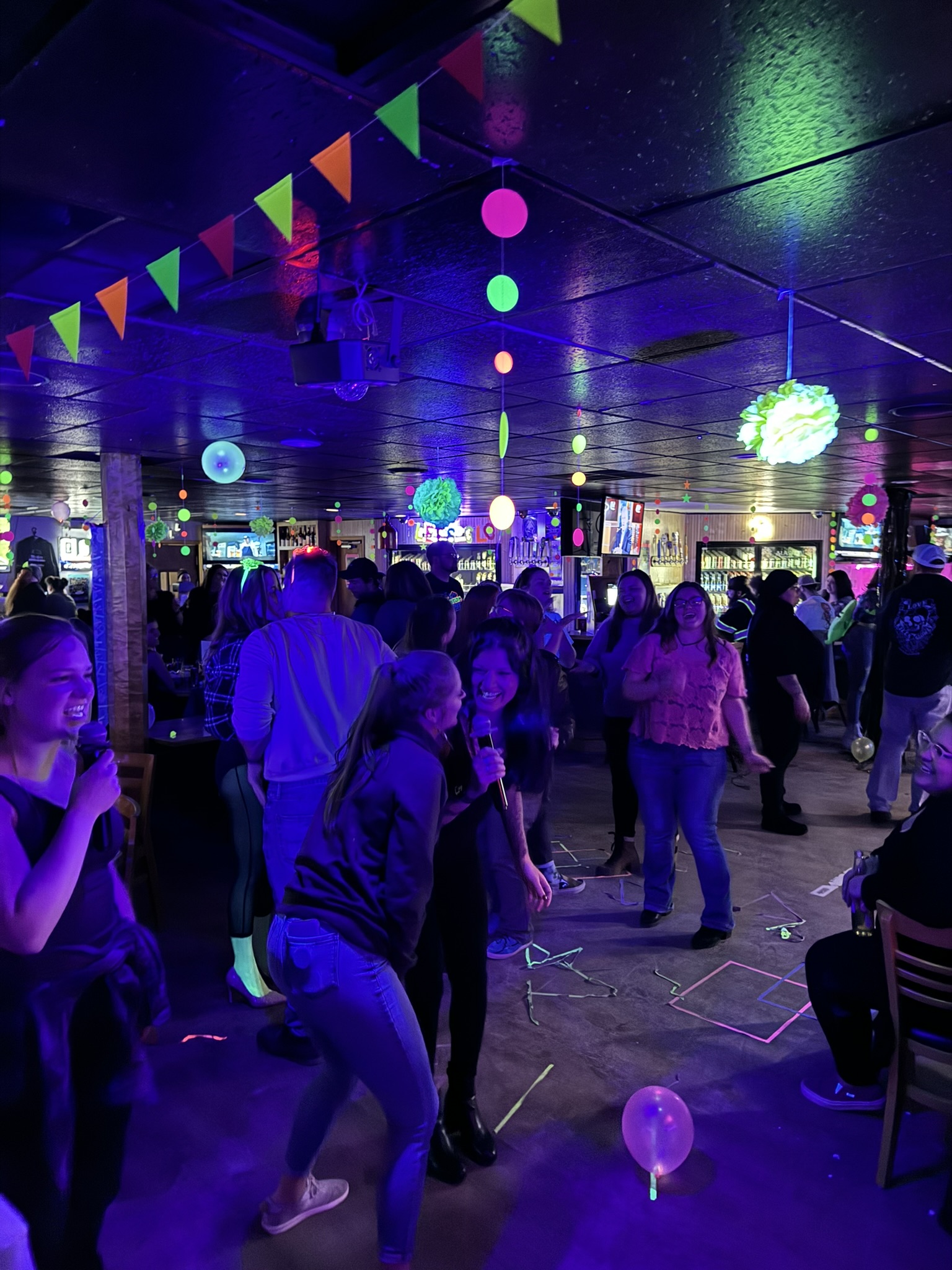 Karaoke night crowd singing and dancing under colorful party lights